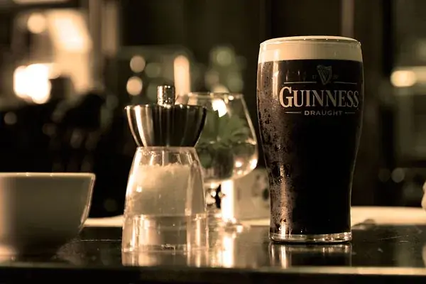 Ein Glas Guinness neben einem Salz- und Pfefferstreuer auf einem Tisch, Bild in Sepiatönen