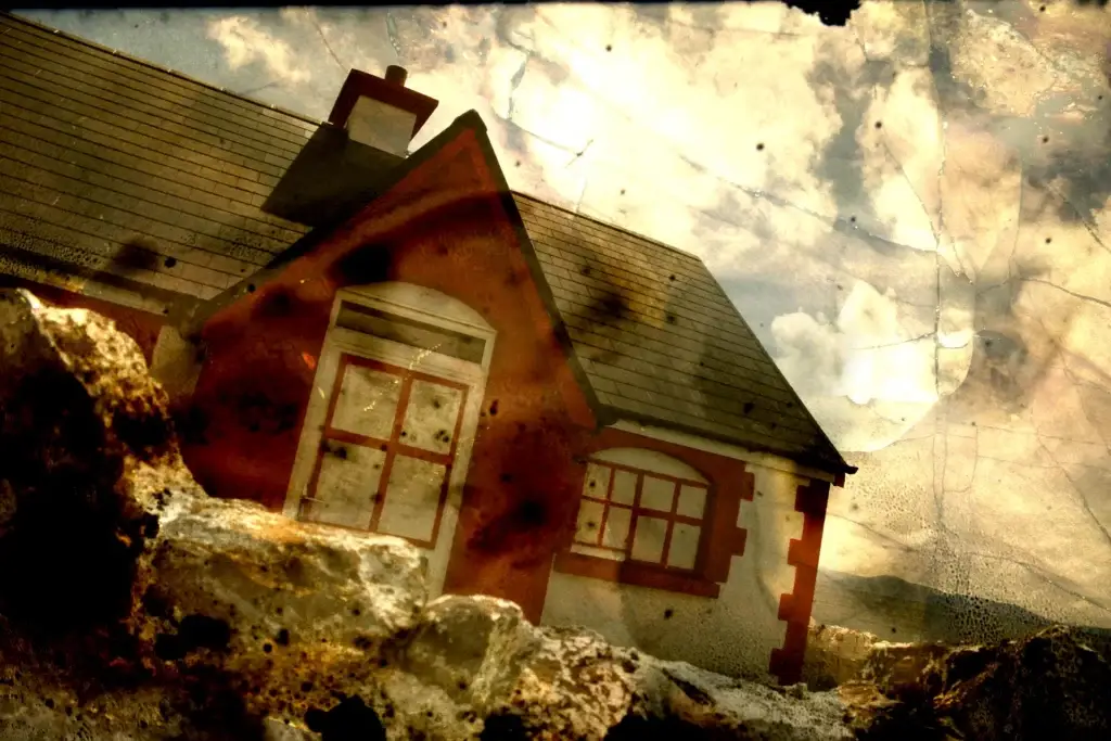 Rotes Haus mit Giebel hinter Felsbrocken, die Wolken sind von feinen Rissen durchzogen